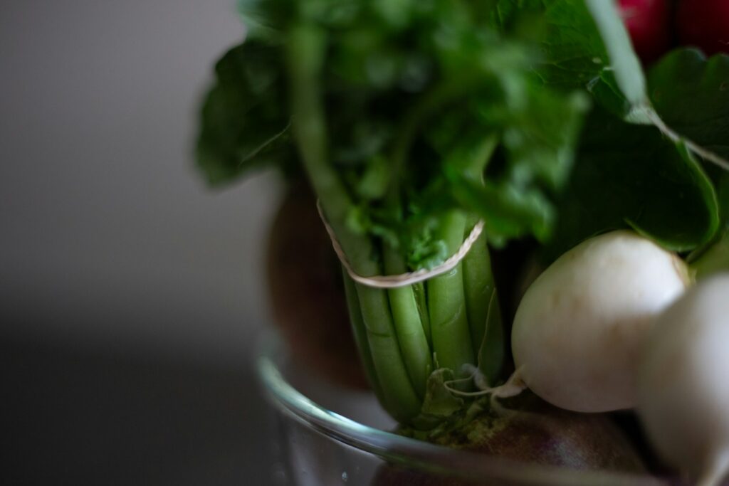a glass bowl filled with green vegetables and radishes