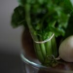 a glass bowl filled with green vegetables and radishes
