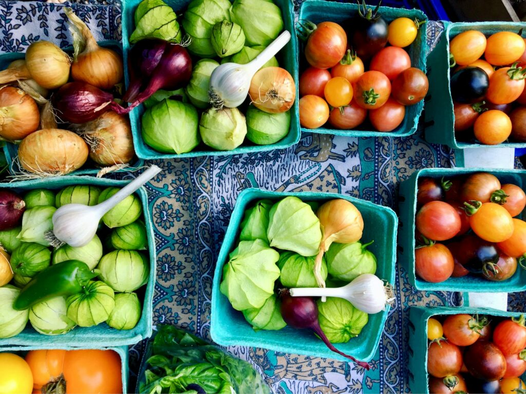 basket of tomato, garlic, and onions on white and blue floral surface